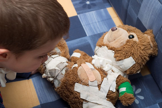 Kind spielt Arzt und klebt Pflaster auf seinen Teddybären